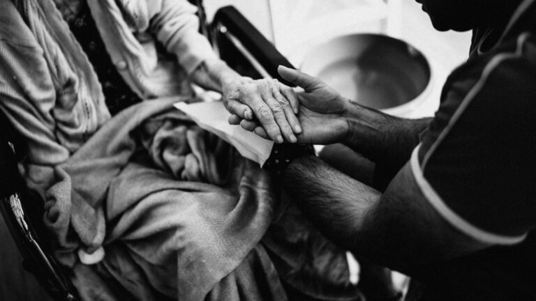 Compassionate support worker holding hands with elderly person
